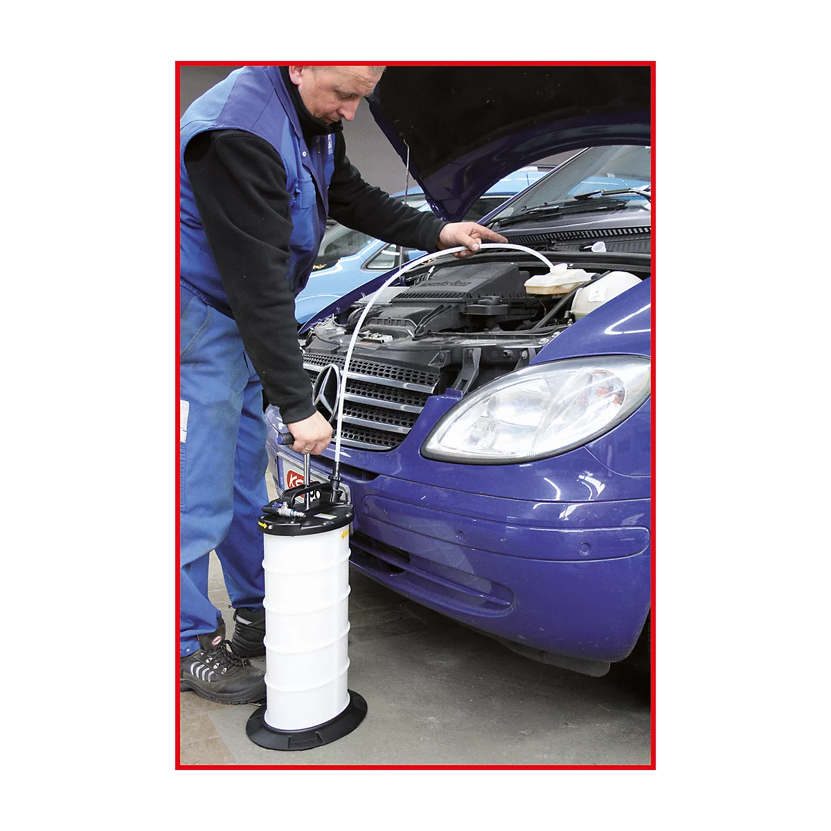 Ein Mechaniker mit Overall und offener Motorhaube arbeitet an einem blauen Auto. Er hält einen weißen Behälter mit einem Schlauch.